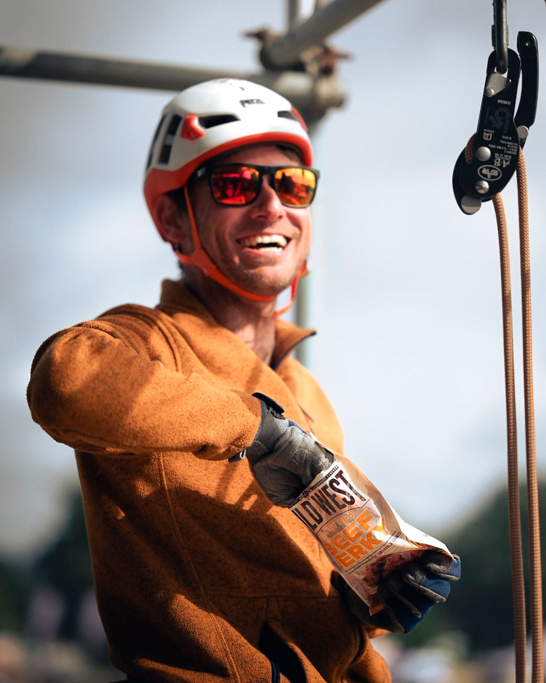 Person in climbing gear with a helmet and gloves, eating from a packet of Wild West Sweet BBQ Beef Jerky