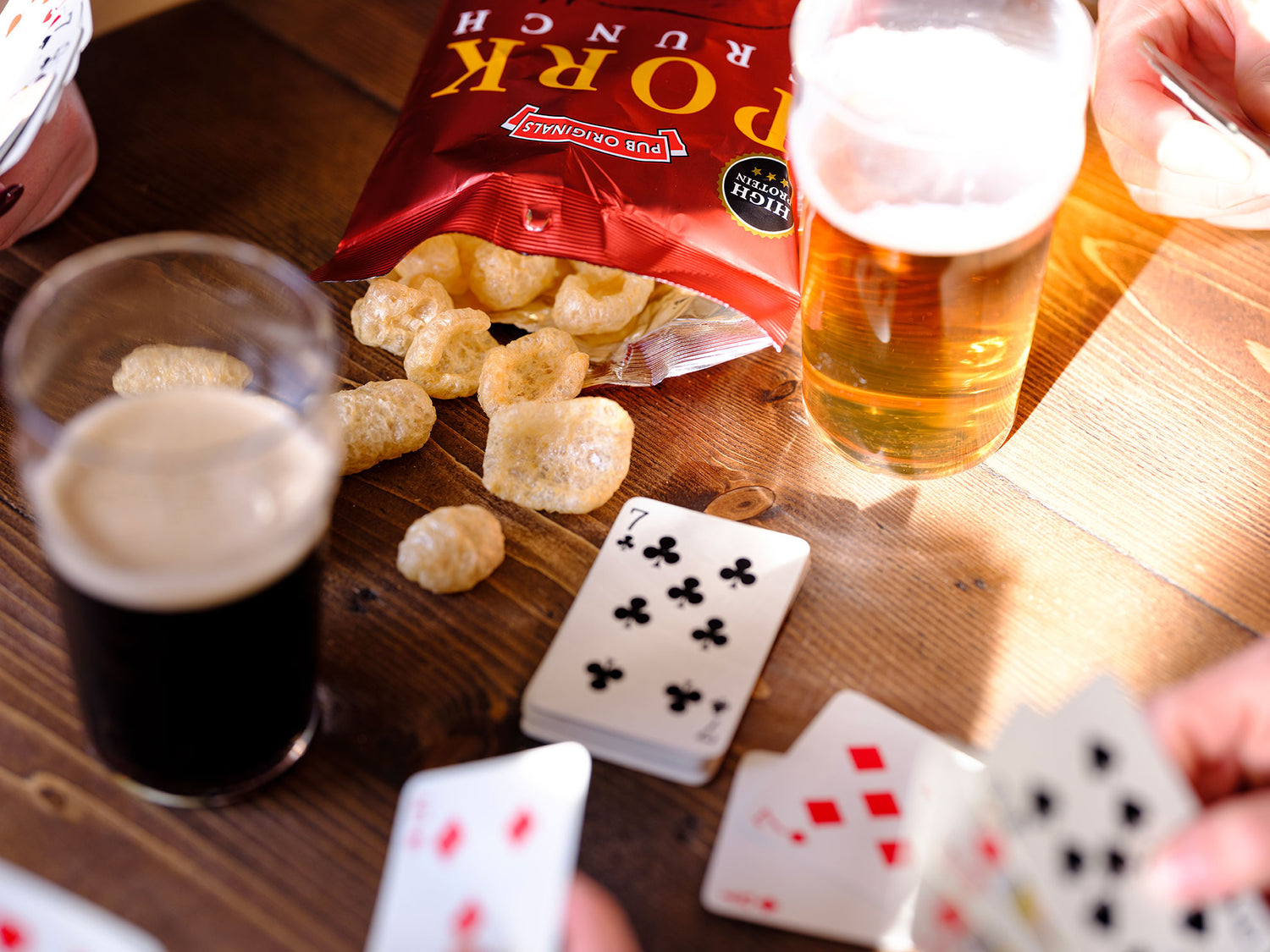 Game of cards with beers and Pub Originals Pork Crunch snacks on a wooden table