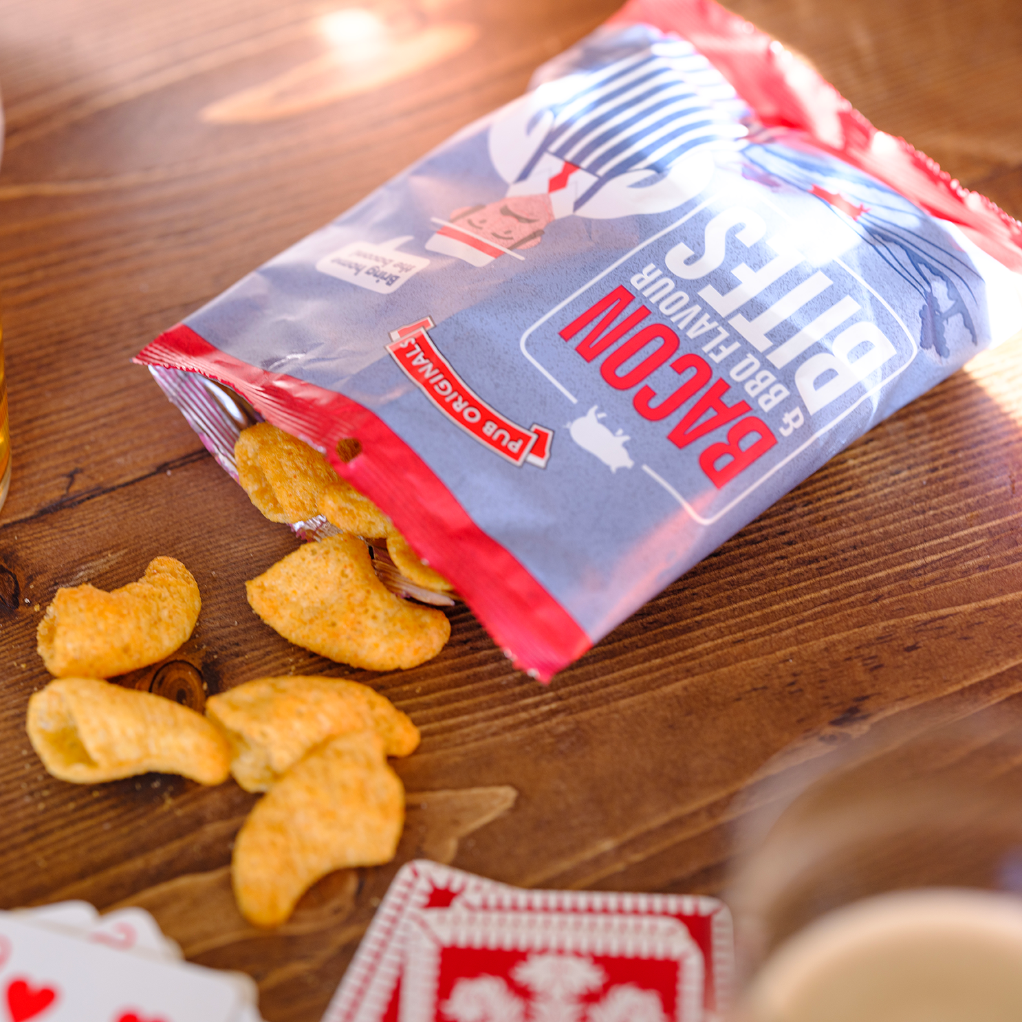Packaged Pub Originals bacon & bbq bites on a wooden table with some bites spilled out.