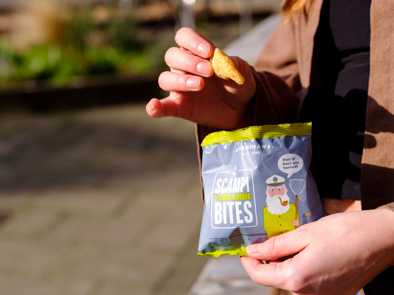 Person holding a packet of Pub Originals Scampi & Lemon Bites with a blurred outdoor background