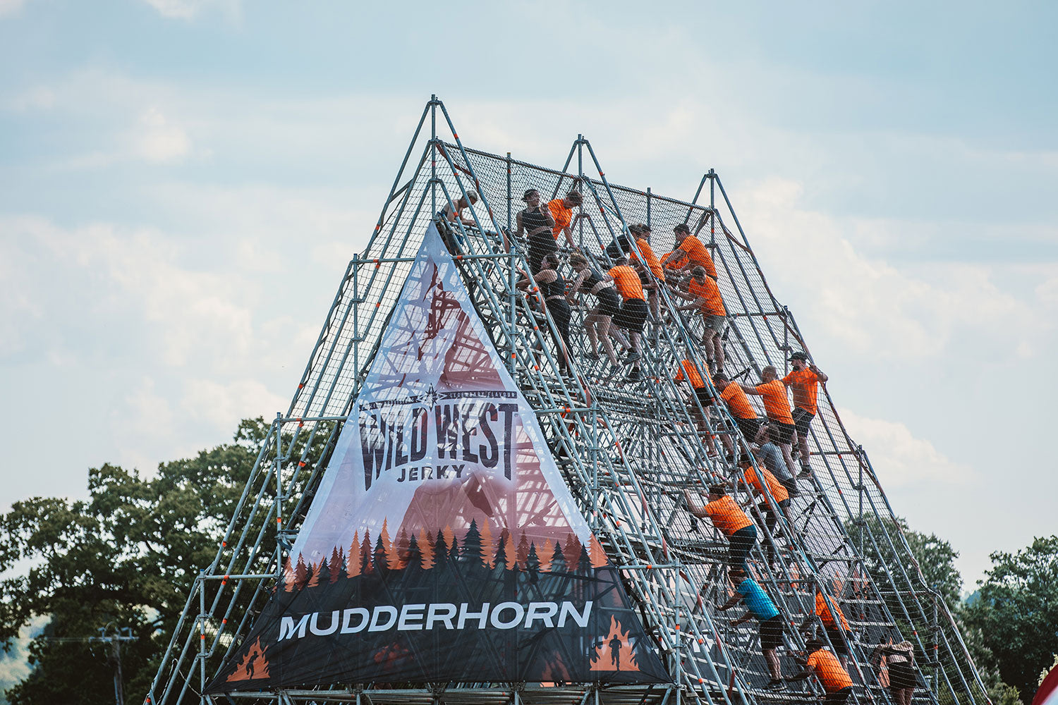 Wild West Jerky sponsor on an obstacle at the Tough Mudder race as people compete to climb over it.