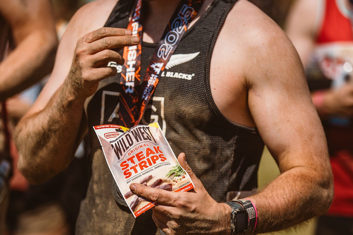Person holding a package of Wild West Steak Strips with a Tough Mudder medal around their neck.